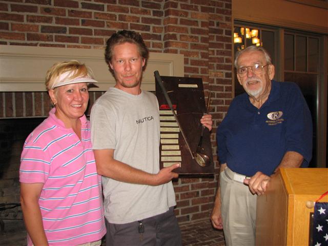 IMG_9273.JPG - Now for the REAL good golfers, there is the competition for the famous “Durfee Award”.  This was named after PP John Durfee when on a particularly bad hole for him years ago … well he had a little tantrum and wrapped his iron around a tree.  It can happen.  He tried to throw the club away … but it was retrieved and mounted ceremoniously on a piece of masonite.  It has been subsequently been awarded to the player with the highest score.  That’s good, right?This year’s award winner at the dinner was Kiwanian Chris Vandermortel.  His name will be memorialized in ink on masking tape, and he must display and care for the plaque until next year when he brings it back to defend his title.  On the left is Past President Jeanne Smith and on the right golf tournament chairman and 2010-2011 club President Jim Leder.  I have to admit I have won that prize in the past.  Congratulations Chris!